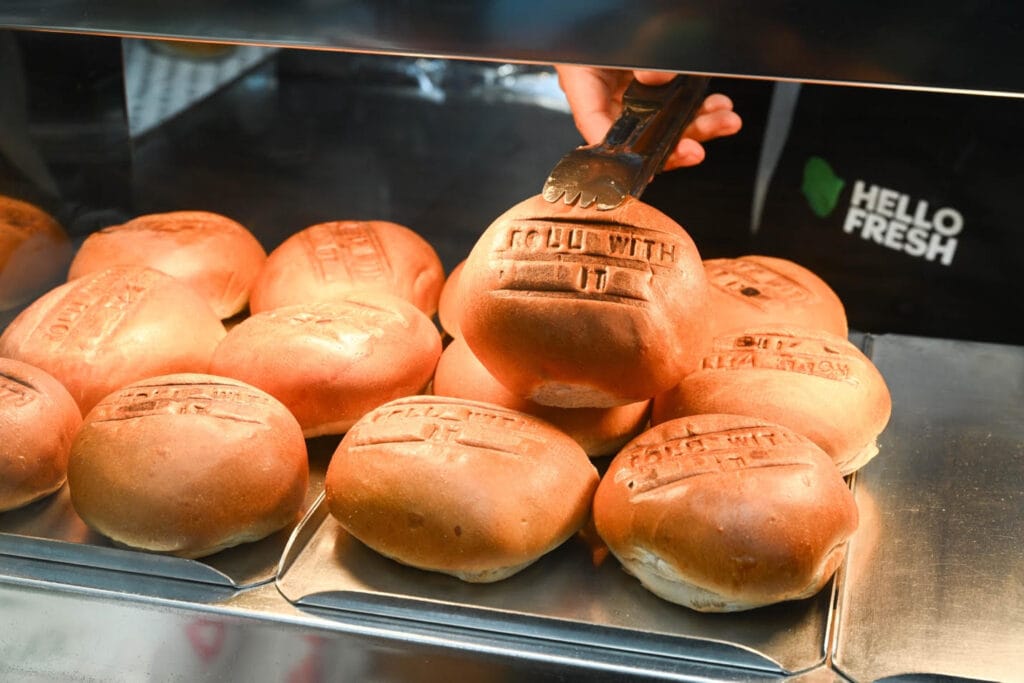 A batch of fresh bread rolls all baked with the words "roll with it" on.
